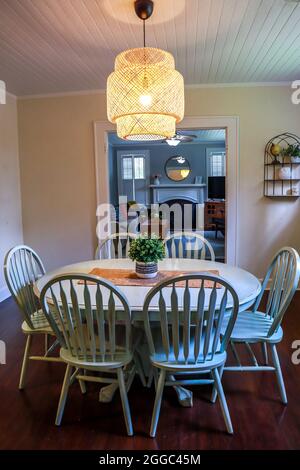 Una piccola sala da pranzo con un'illuminazione in rattan di tendenza e un tavolo da pranzo dipinto di blu Foto Stock