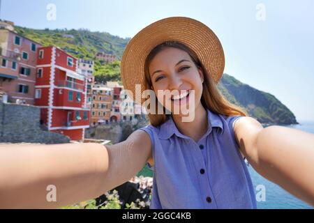 Sorridente ragazza turistica scattando foto selfie nella giornata di sole a Riomaggiore, cinque Terre, Italia Foto Stock