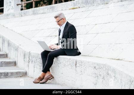 Computer portatile per uomini d'affari mentre si siede sulle scale nel centro della città Foto Stock
