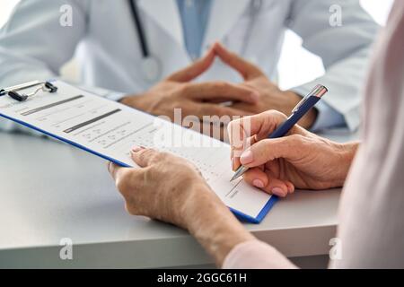 Closeup paziente anziano riempire il modulo dei dati sanitari in clinica ospedaliera. Foto Stock