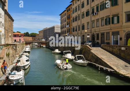 Una piccola barca che naviga su un canale del quartiere Venezia Nuova nel centro storico di Livorno in una giornata estiva soleggiata, Toscana, Italia Foto Stock