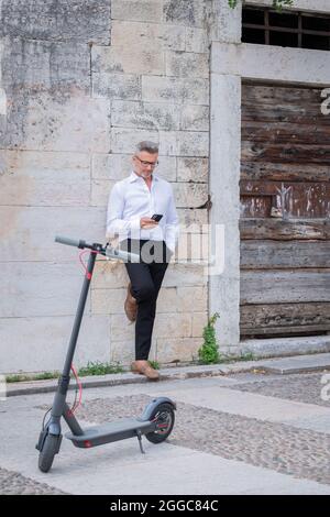 Giovane uomo d'affari che usa il telefono vicino a scooter elettrico. Concentrarsi sullo scooter Foto Stock