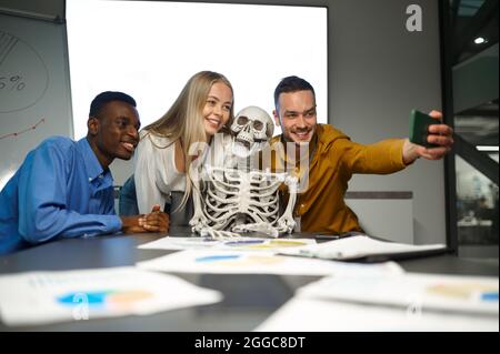 Gestori divertenti, selfie con scheletro in ufficio IT Foto Stock