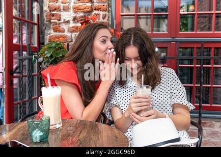 due ragazze belle giovani seduti in un caffè urbano con caffè e la condivisione di segreti, ragazze partito concetto Foto Stock