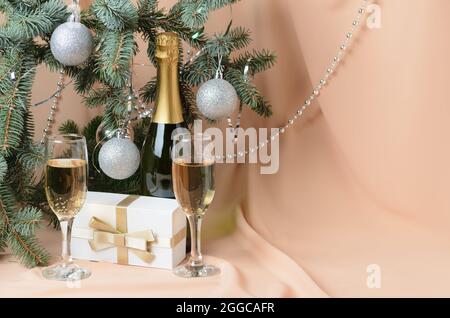 Natale. Una composizione di Capodanno fatta di rami di un albero di Natale decorato con palle d'argento, una scatola regalo, bicchieri di vino frizzante su uno sfondo Foto Stock