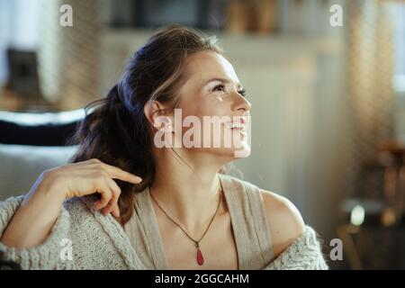 sorridente donna moderna in maglia accogliente cardigan nel soggiorno moderno in soleggiata giornata invernale. Foto Stock