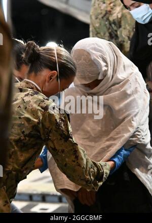 210828-N-OX321-1085 STAZIONE AERONAVALE DI SIGONELLA, ITALIA (AGOSTO 28, 2021) Naval Air Station Sigonella Command Master Chief Anna Wood assiste una donna afghana giù da un Boeing US Air Force C-17 Globemaster III portando evacuati dall'Afghanistan alla Naval Air Station Sigonella, 28 agosto 2021. NAS Sigonella sta attualmente supportando la missione del Dipartimento di Stato per facilitare la partenza e il trasferimento in sicurezza dei cittadini degli Stati Uniti, dei beneficiari di visti speciali per l'immigrazione e delle popolazioni vulnerabili provenienti dall'Afghanistan. (STATI UNITI Foto Navy di Mass Communication Specialist 1a classe Kegan E. Kay) Foto Stock