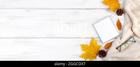 Ciao autunno. Foglie gialle, blocco note e bicchieri. Spazio di lavoro elegante. Composizione piatta su sfondo bianco di legno. Spazio di copia. Foto Stock