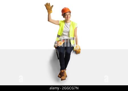 Ritratto a tutta lunghezza di una allegra ingegnere femminile seduto su un pannello vuoto e ondeggiante isolato su sfondo bianco Foto Stock