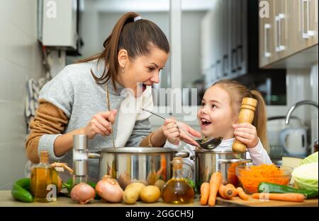 Madre emozionale e piccola figlia degustazione zuppa insieme Foto Stock