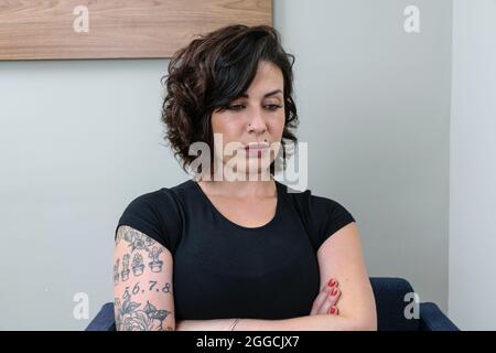 Donna brasiliana, tatuata, con le braccia incrociate e guardando verso il basso. Premuroso e sconvolto. Foto Stock