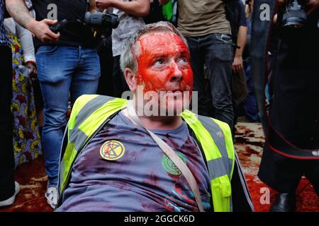 Londra, Regno Unito. Un manifestante della ribellione dell'estinzione che partecipa alla marcia "Blood Money" del gruppo si siede con sangue falso sul suo volto Foto Stock