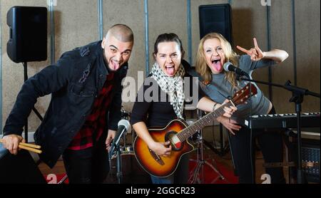 Tre bandmates che si posano insieme a strumenti musicali nella sala delle prove Foto Stock