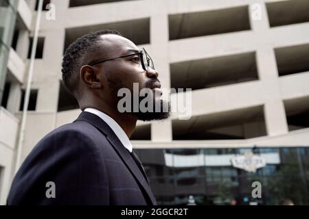 Vista laterale di un giovane uomo d'affari serio di etnia africana che si oppone all'architettura moderna Foto Stock