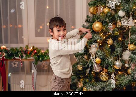 Ragazzo sorridente che appende la palla sull'albero di natale Foto Stock