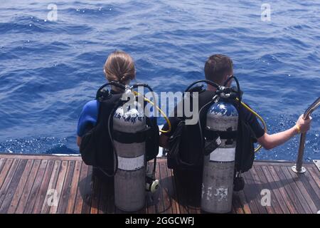 un uomo e una donna con attrezzatura subacquea in tute si stanno preparando a tuffarsi in acqua. Foto Stock