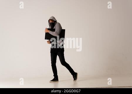 Un uomo con un monitor nelle sue mani ruba un computer anonimato Hacker Studio Foto Stock