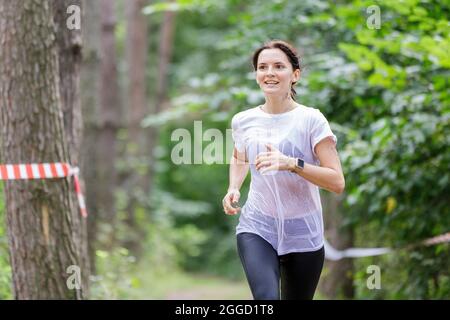 Giovane sportivo bagnato che corre sul suo corso in gara di ostacolo dopo aver attraversato un fiume Foto Stock