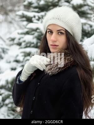 Giovane ragazza allegra in piedi fuori nella neve in berlina a maglia e guanti bianchi Foto Stock