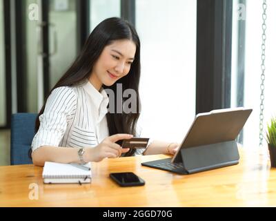 Shopping online, concetto di e-commerce, giovane donna attraente che paga con carta di credito tramite sito web di shopping online, utilizzando tablet digitale Foto Stock