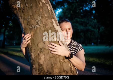 mano donna che abbraccia un albero nella foresta - la natura che ama, combattere il riscaldamento globale, salvare il pianeta terra Foto Stock