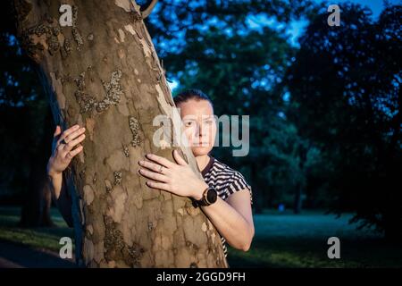 mano donna che abbraccia un albero nella foresta - la natura che ama, combattere il riscaldamento globale, salvare il pianeta terra Foto Stock