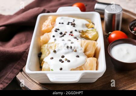 Piatto da forno con gustosi involtini di cavolo ripieni e salsa sul tavolo Foto Stock