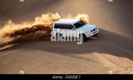 un'auto bianca o suv sta salendo da una duna di sabbia e spruzza sabbia sull'aria e intorno in dasht e lut o sahara deserto. ads spazio Foto Stock