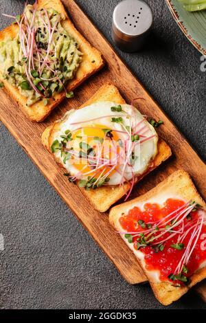 Asse di legno con deliziosi toast su sfondo scuro, primo piano Foto Stock