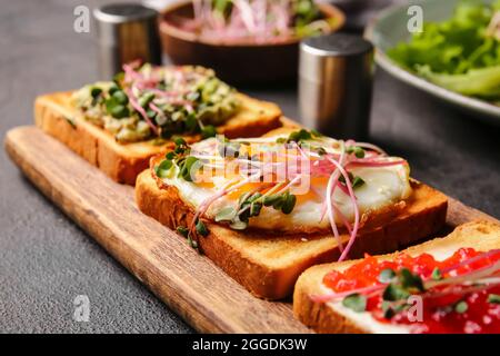 Asse di legno con deliziosi toast su sfondo scuro, primo piano Foto Stock