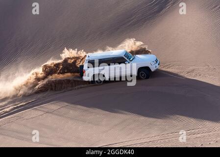 un'auto bianca o suv sta salendo da una duna di sabbia e spruzza sabbia sull'aria e intorno in dasht e lut o sahara deserto. ads spazio Foto Stock