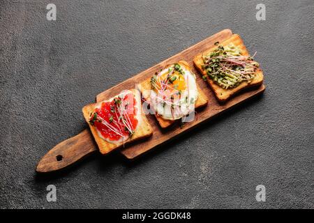 Asse di legno con deliziosi toast su sfondo scuro Foto Stock