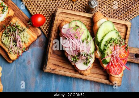 Tavole di legno con gustosi croissant e toast con micro verde su sfondo di legno colorato Foto Stock