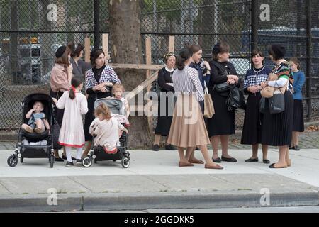 Un gruppo di madri e famiglie ebraiche ortodosse vestite modestamente aspetta un autobus scolastico per arrivare con i loro figli. A Williamsburg, Brooklyn, New York. Foto Stock