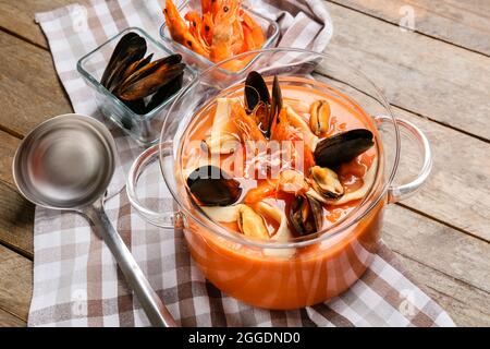 Pentola di gustosa zuppa di Cacciucco e ingredienti su sfondo di legno Foto Stock