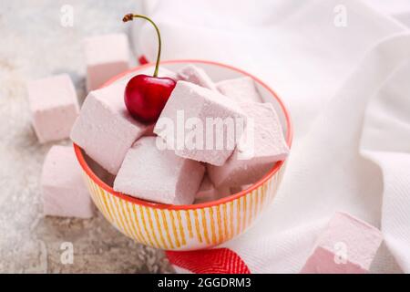 Ciotola con gustose marshmallows dolci e ciliegia su sfondo chiaro Foto Stock