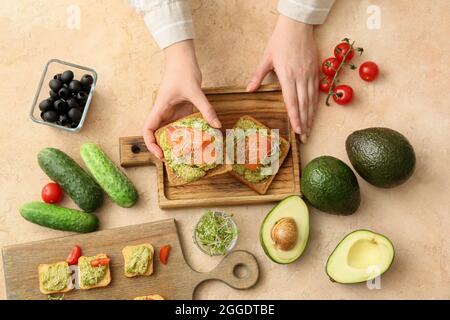Donna che tiene gustosi sandwich con guacamole e salmone a tavola Foto Stock