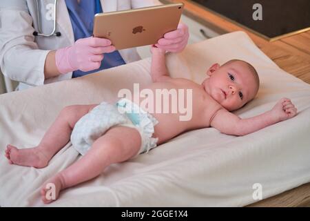 Medico pediatra in possesso di iPad di mela e neonato. Infermiera in uniforme con bambino e tablet digitale - Mosca, Russia, 17 agosto 2021 Foto Stock