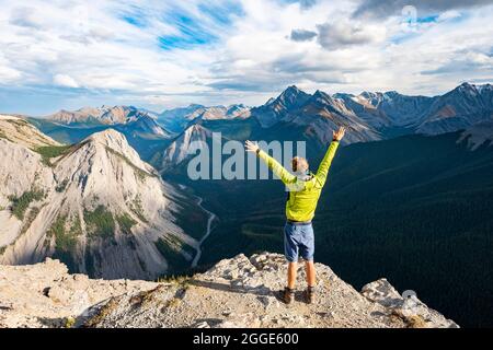 Escursionista allunga le braccia in aria, paesaggio di montagna con valle del fiume e cime, cime con giacimenti di zolfo arancio, rovesciamento montagna, panoramica Foto Stock