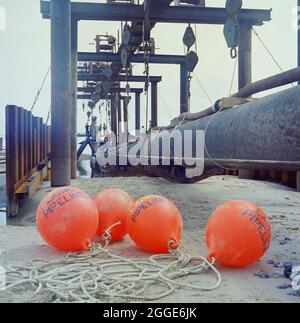 Una vista del sito di lancio del gasdotto North Coates, che mostra le boe dei gasdotti di Laing in primo piano con il gasdotto e le attrezzature di sollevamento in background. I lavori di ingegneria civile sul gasdotto North Coates sono stati eseguiti da Laing Pipelines insieme alle società francesi Entrepose e GTM, e il principale appaltatore per i lavori di dragaggio era Dreging and Construction Company insieme ad Adriaan Volker di Rotterdam. Oltre due miglia di 36 pollici di diametro pipeline, racchiusi in calcestruzzo, è stato tirato fuori in mare nell'estuario dell'Humber il 16 giugno 1970. Foto Stock