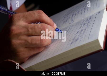 Un uomo sta scrivendo con una penna blu su un fuoco di notebook.selective Foto Stock