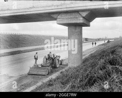 Una vista dei lavori di ricostruzione delle spalle dure sulla M1, l'autostrada da Londra a Yorkshire, che mostra una macchina dello stabilizzatore multipasso al lavoro sotto di un ponte. La didascalia dell'album fa riferimento a questa immagine come alla "London/Birmingham Motorway". Foto Stock