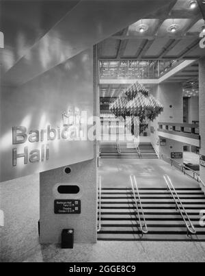 Una vista da un alto punto panoramico del foyer principale nel Centro Barbican di recente apertura, che mostra una scultura sospesa sopra la scala e l'ingresso per la Sala Barbican. Questa immagine è stata scattata poco dopo l'apertura del Centro Barbican mercoledì 3 marzo 1982. Il Centro Barbicano fu aperto cerimonialmente dalla Regina Elisabetta II, che svelò una targa commemorativa per segnare l'occasione. La scultura di questa immagine, disegnata da Michel Santry, è sospesa a un lucernario sopra le scale. La scultura ha la forma di un ottaedro ed è costruita da sei gruppi a nido d'ape d'oro p. Foto Stock