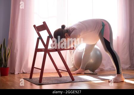 Donna incinta che fa inversione gamba diffusa intensa Prasarita Padottanasana yoga posa a casa Foto Stock