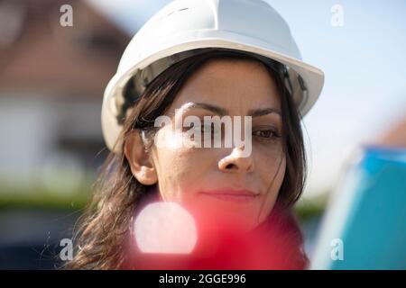 Donna di mezza età con capelli scuri e casco controlla una pianta con una tavoletta, Friburgo, Baden-Wuerttemberg, Germania Foto Stock