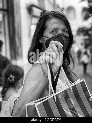 Scatto verticale in scala di grigi di una donna caucasica di mezza età che indossa una maschera e tiene una borsa Foto Stock