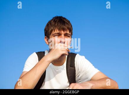 Sad Young Man fumante sigaretta sullo sfondo del cielo Foto Stock