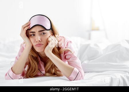 Stanco turbato annoiato signora svegliarsi dopo cattivo sonno, stanco o insonne. Sconvolto triste infelice bella millenaria europea femmina in rosa pajama e dormire ma Foto Stock