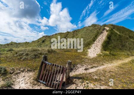 Alta duna coltivata di erba, ingresso attraverso un cancello di legno Foto Stock