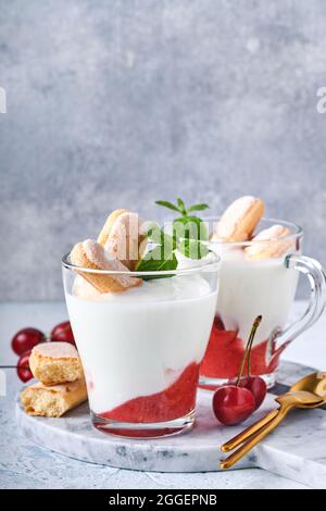 Pasta sfoglia estiva con biscotti savoiardi e formaggio cremoso in vetro su fondo grigio chiaro. Tradizionale torta tiramisù con frutti di bosco freschi. SEL Foto Stock